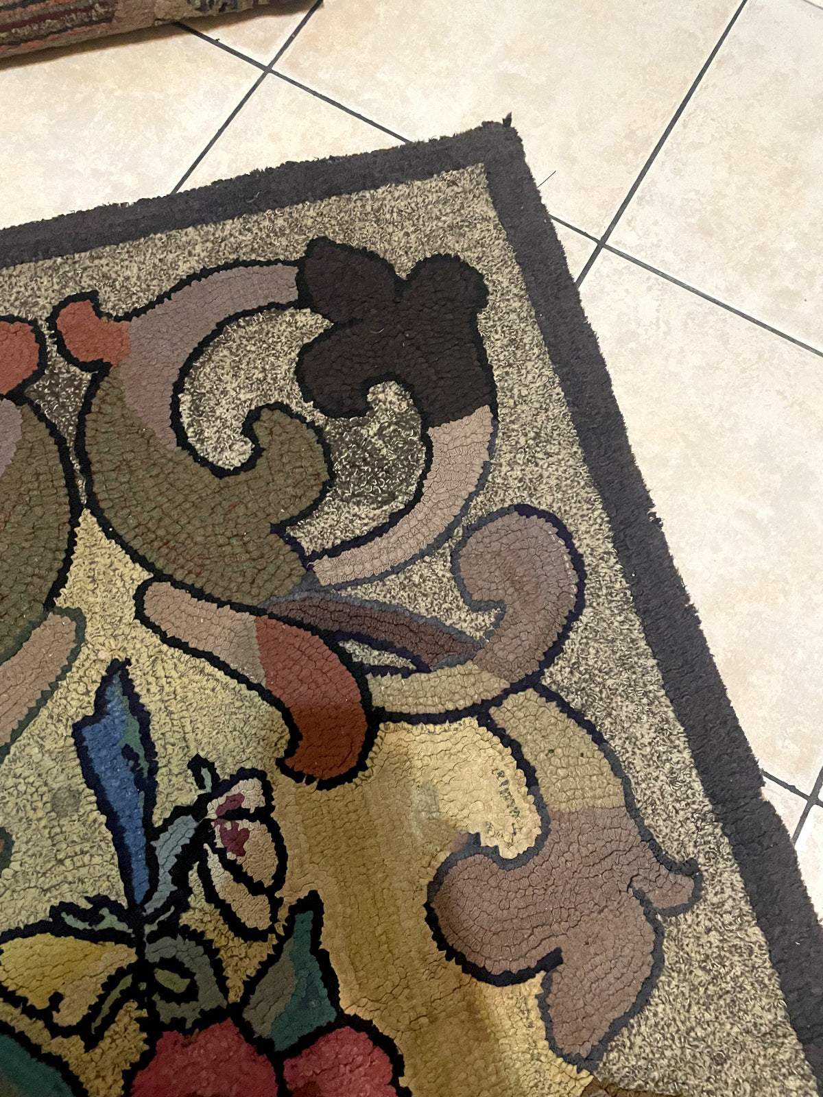 Detail of the central floral bouquet on a vintage American hooked rug, featuring magenta and crimson roses outlined in black against a warm golden-ivory background.

