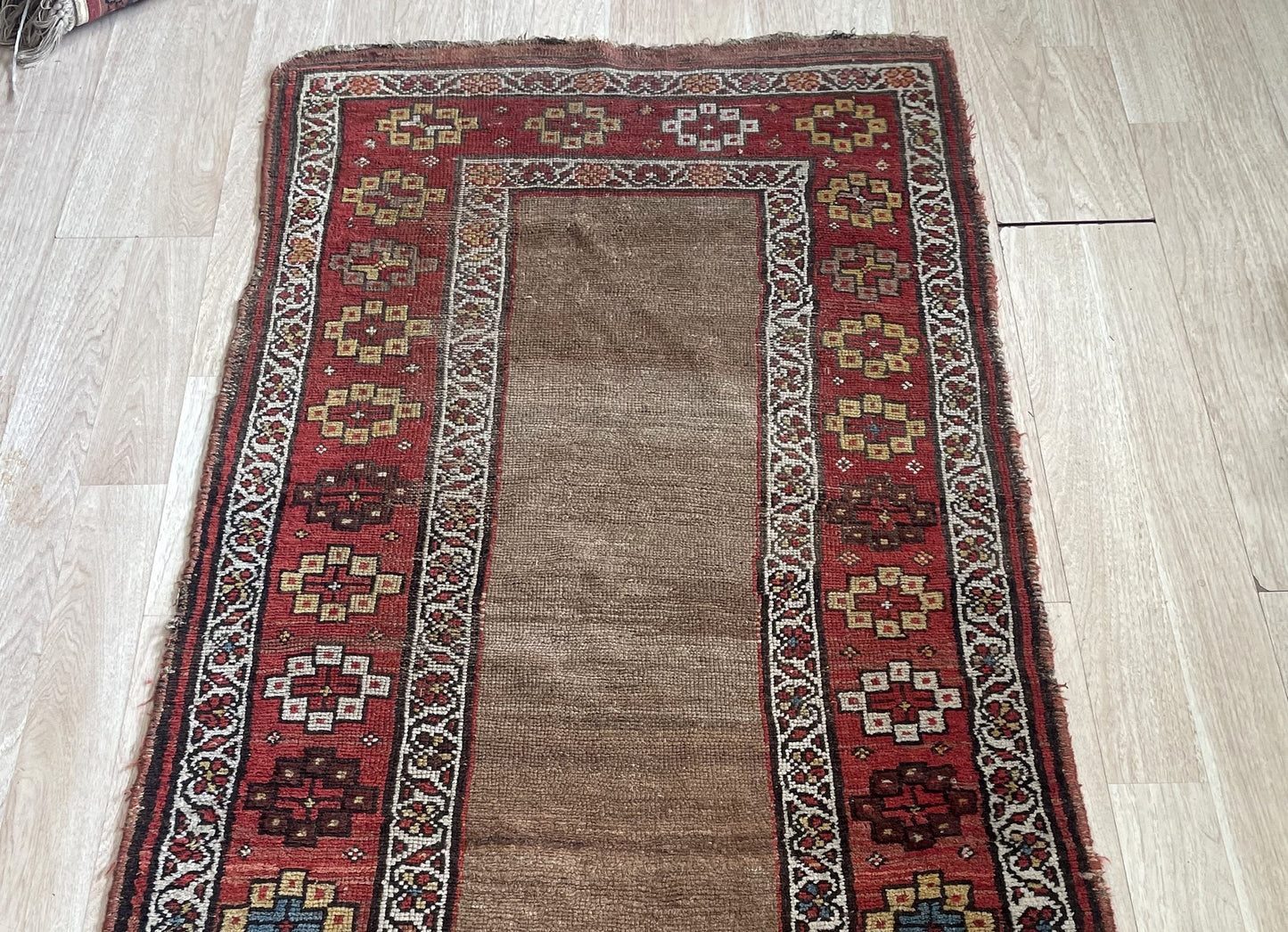 Antique Kurdish tribal runner measuring 2'7" x 6'3" with an open camel ground, deep burgundy border system, and honest age wear including low pile areas and consumed fringe.

