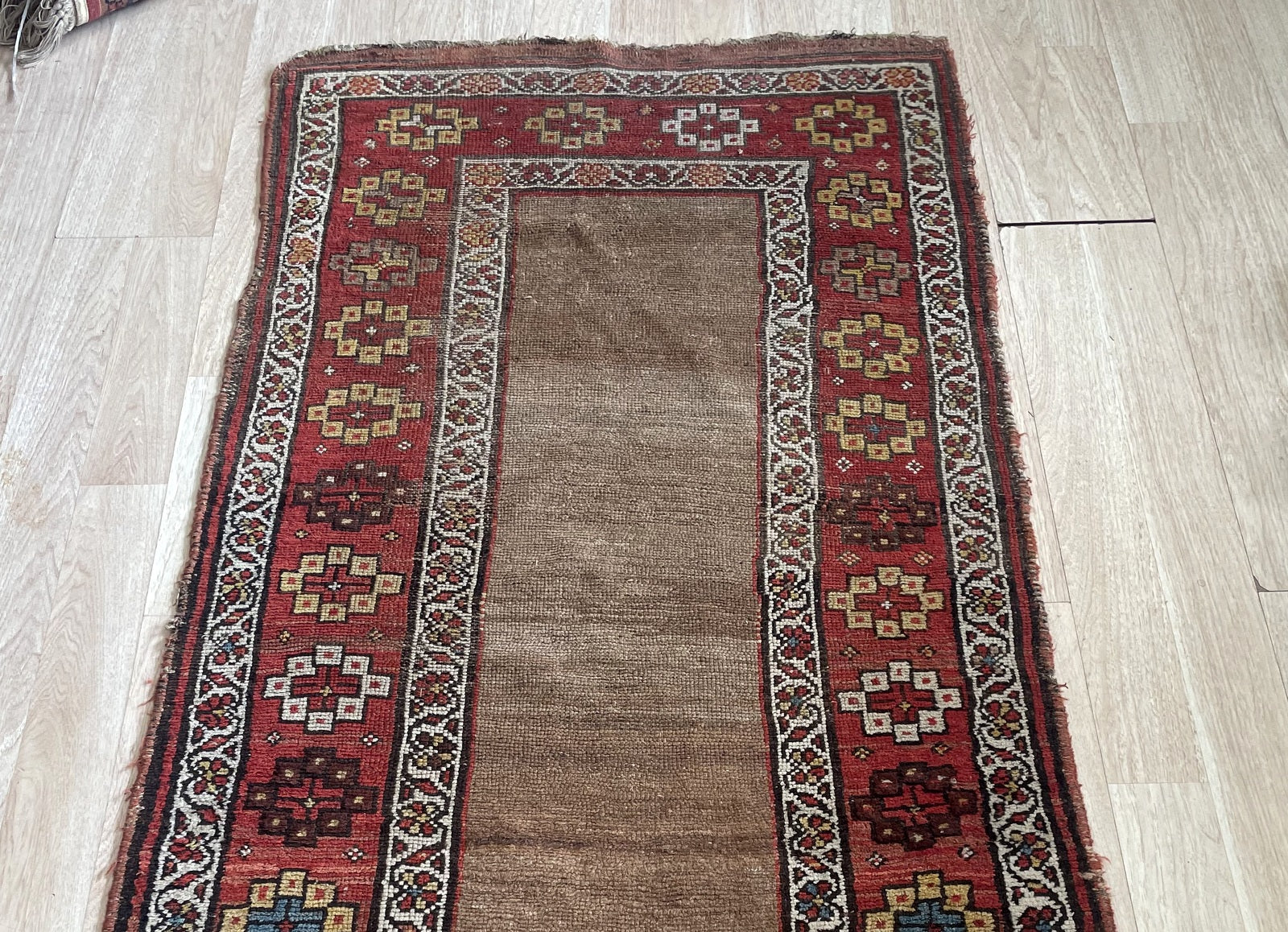Antique Kurdish tribal runner measuring 2'7" x 6'3" with an open camel ground, deep burgundy border system, and honest age wear including low pile areas and consumed fringe.

