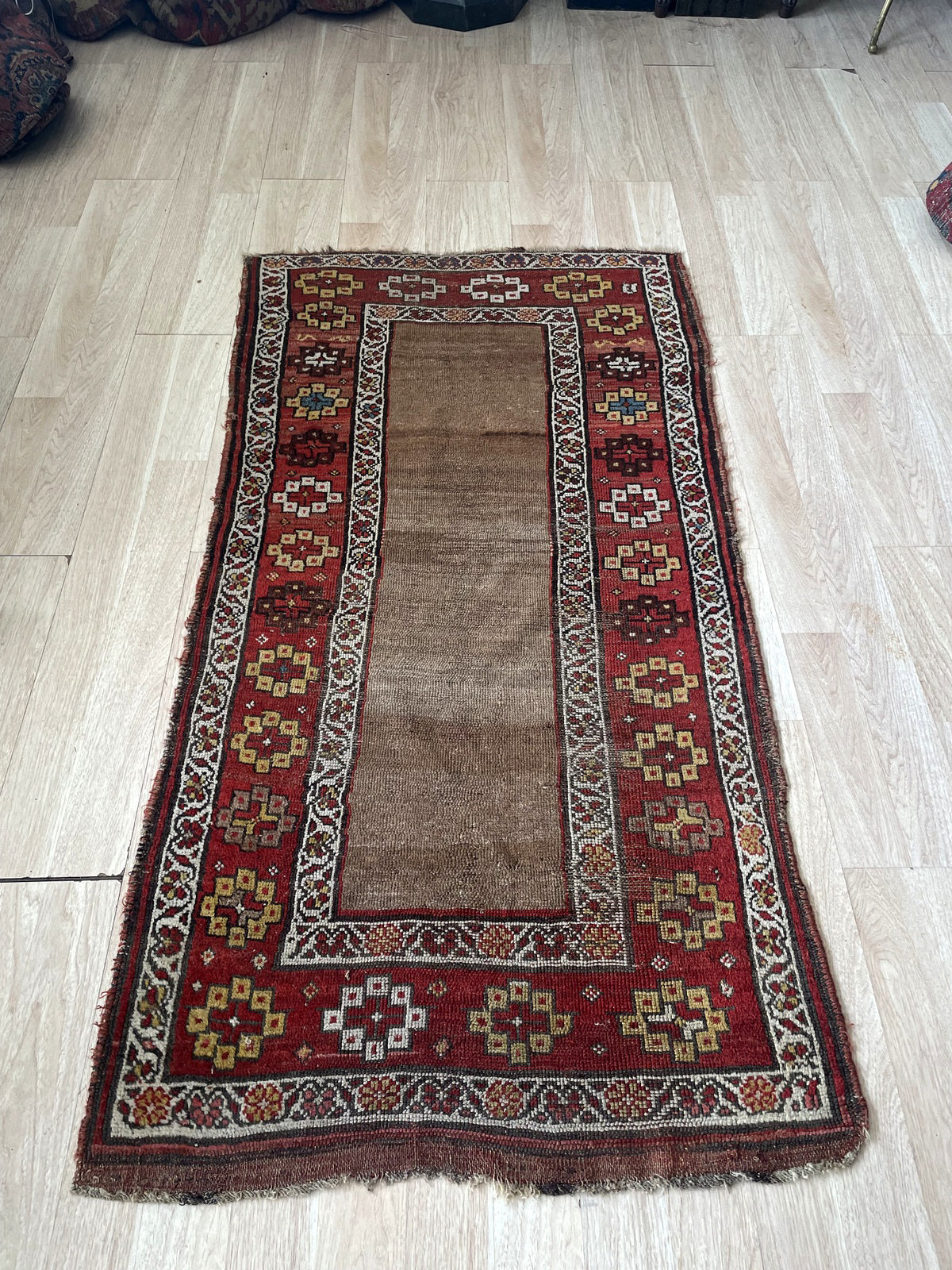 Detail of the main border on an 1870s Kurdish tribal rug, showing continuous and varied hooked diamond medallions, star rosettes, and stepped forms against a deep crimson background.

