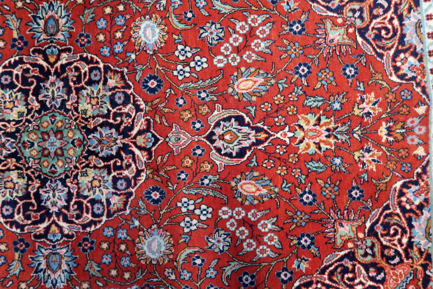 Close-up of the red background with floral motifs on the handmade antique Persian Kashan rug.