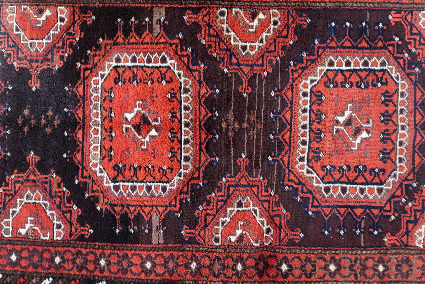 Close-up of the deep chocolate brown motifs contrasting against the red field.


