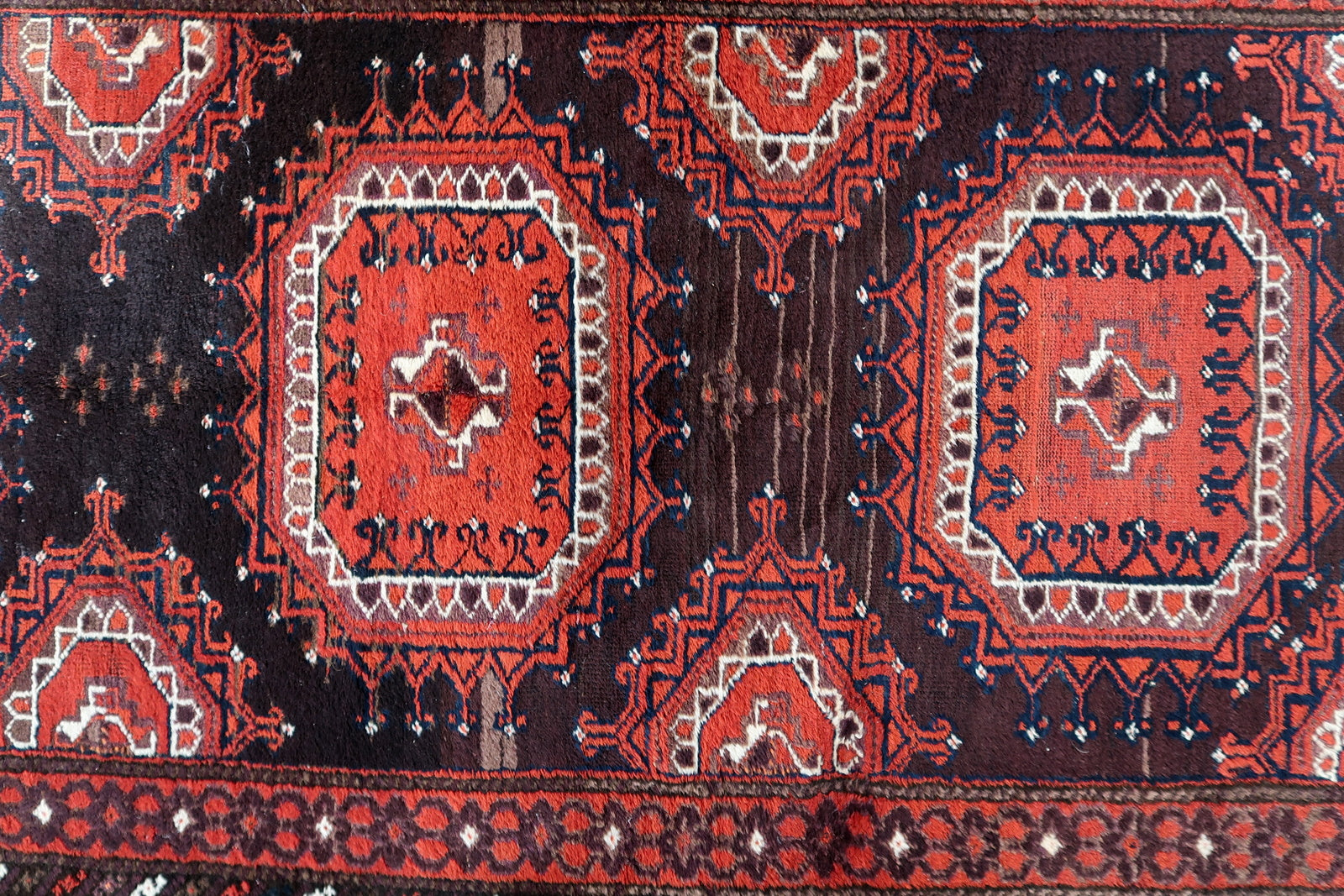 Close-up of the deep chocolate brown motifs contrasting against the red field.

