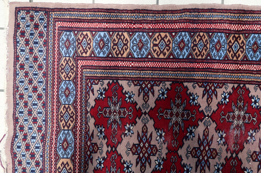 Hand-knotted tribal wool rug from Uzbekistan with rich crimson red medallions and intricate blue and gold geometric borders.


