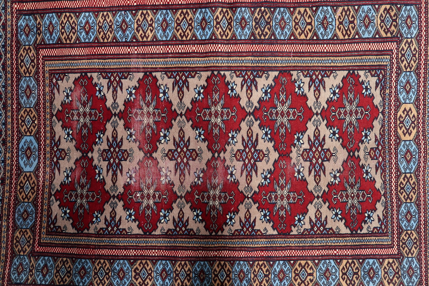 Close-up of a Central Asian tribal rug with a mesmerizing geometric pattern of red diamonds on a worn beige wool foundation.

