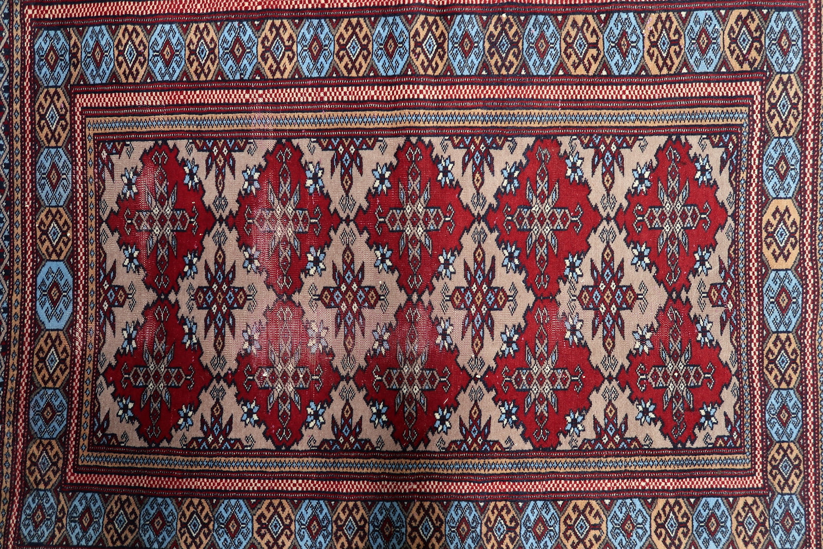 Close-up of a Central Asian tribal rug with a mesmerizing geometric pattern of red diamonds on a worn beige wool foundation.

