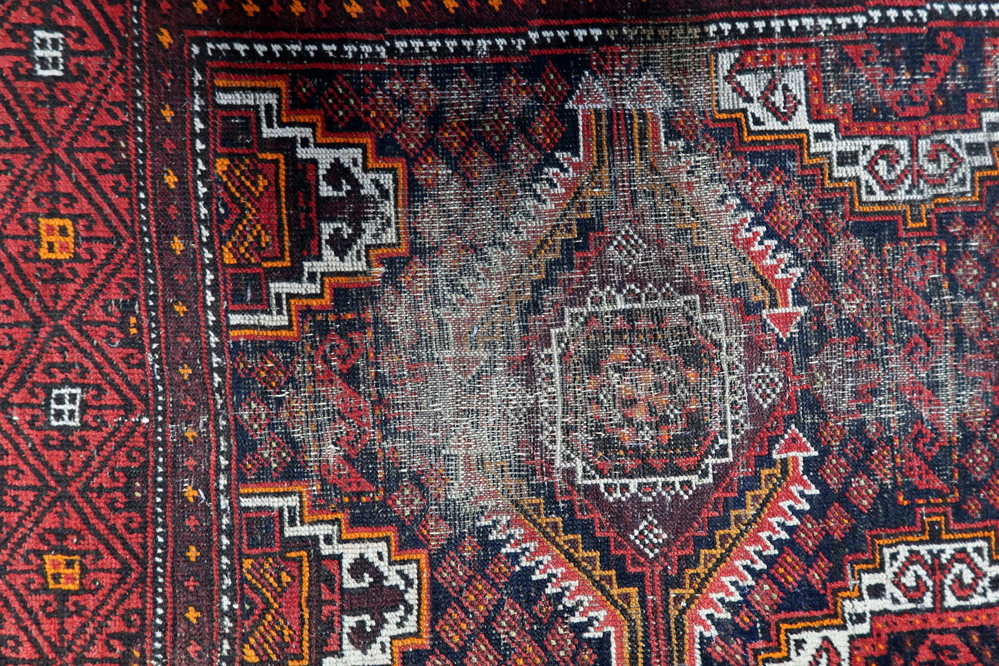 Close-up of a Central Asian tribal rug with angular hooked diamonds and intricate interior geometric patterns.

