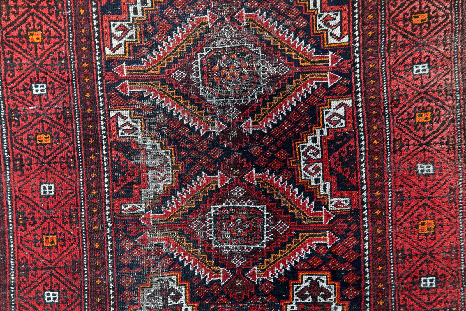 Traditional Baluch tribal weaving with wide geometric borders and repeating diamond and cross motifs.

