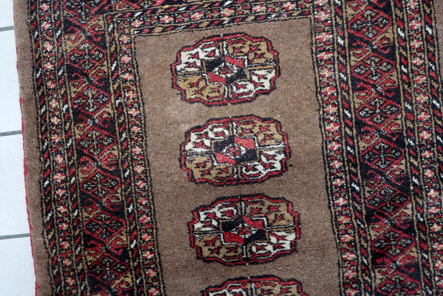 Close-up of a Central Asian tribal rug with repeating crimson medallions filled with geometric patterns.

