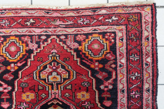 Hand-knotted wool village rug with bold geometric and floral motifs in crimson, orange, pink, and navy.

