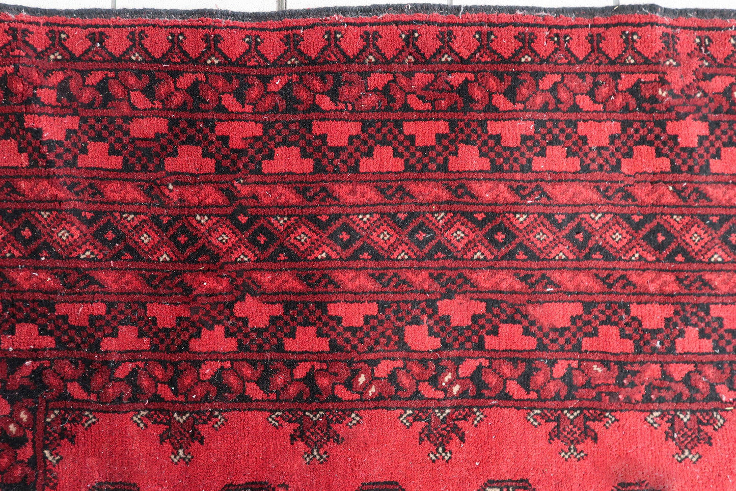 Detail view of the mesmerizing pattern on a 100-year-old Ersari rug, showing repeating geometric medallions across a luminous coral-red field.

