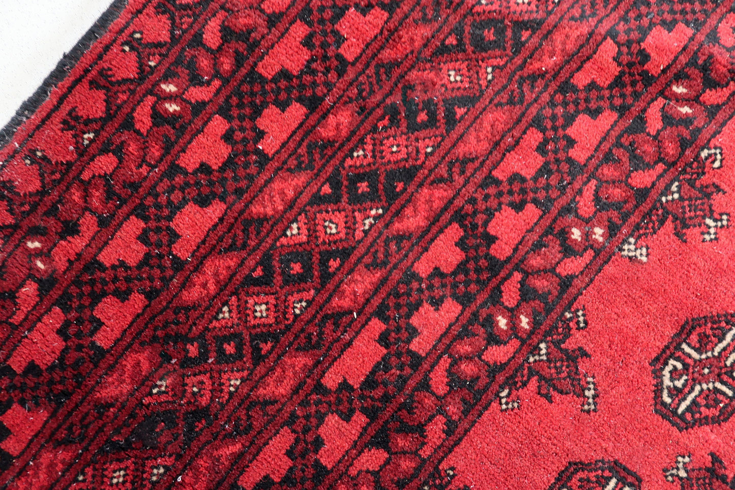 Intricate geometric borders on an antique Turkmen rug, featuring wide bands with diamond and latch-hook motifs framed by narrow guard stripes.

