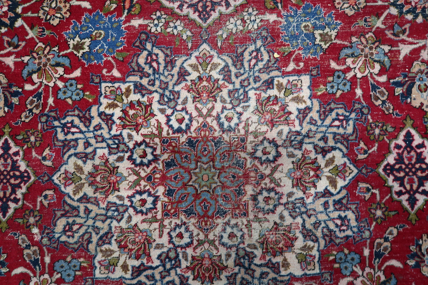 Subtle central medallion emerging from the dense crimson red field of an antique Persian city rug.

