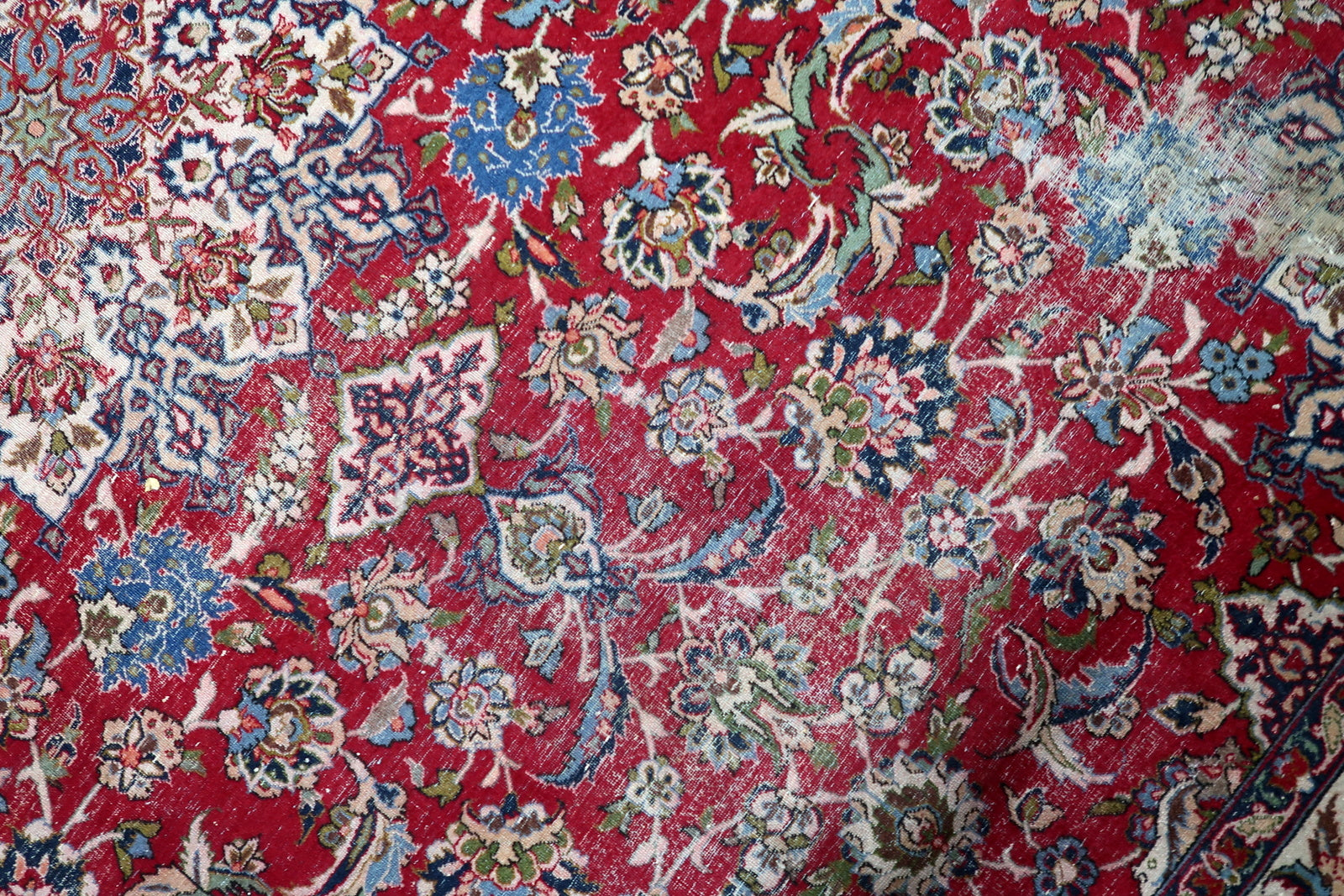 Color palette detail of an antique Persian carpet: crimson red ground with accents of sky blue, beige, cream, and green.

