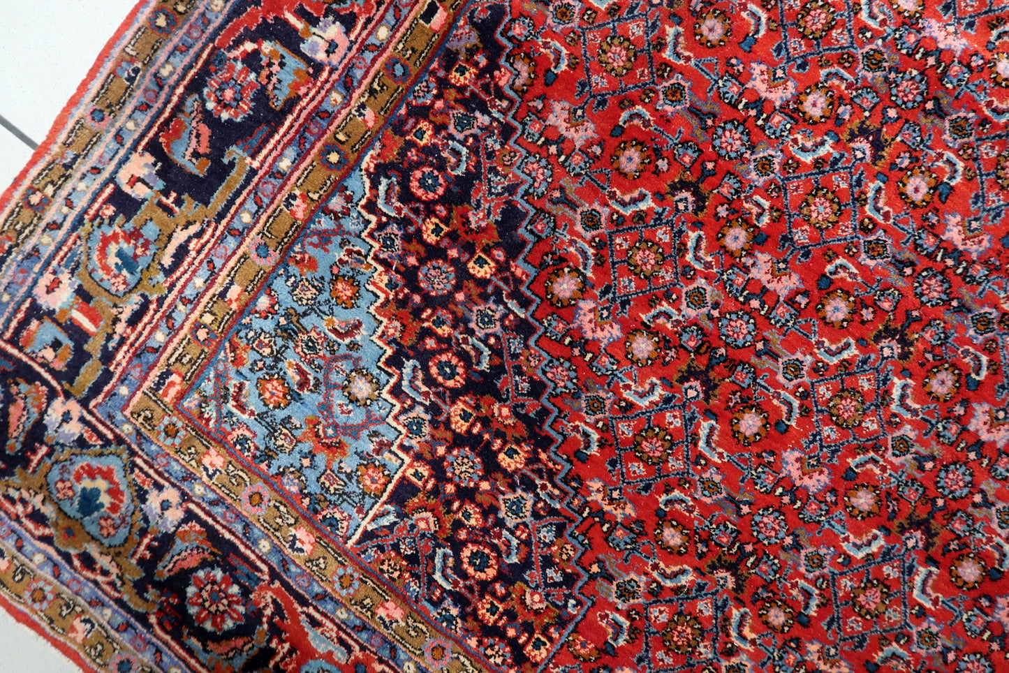 Close-up of the central diamond medallion on an antique Persian Bidjar rug, featuring sky blue and ivory tones against madder red.

