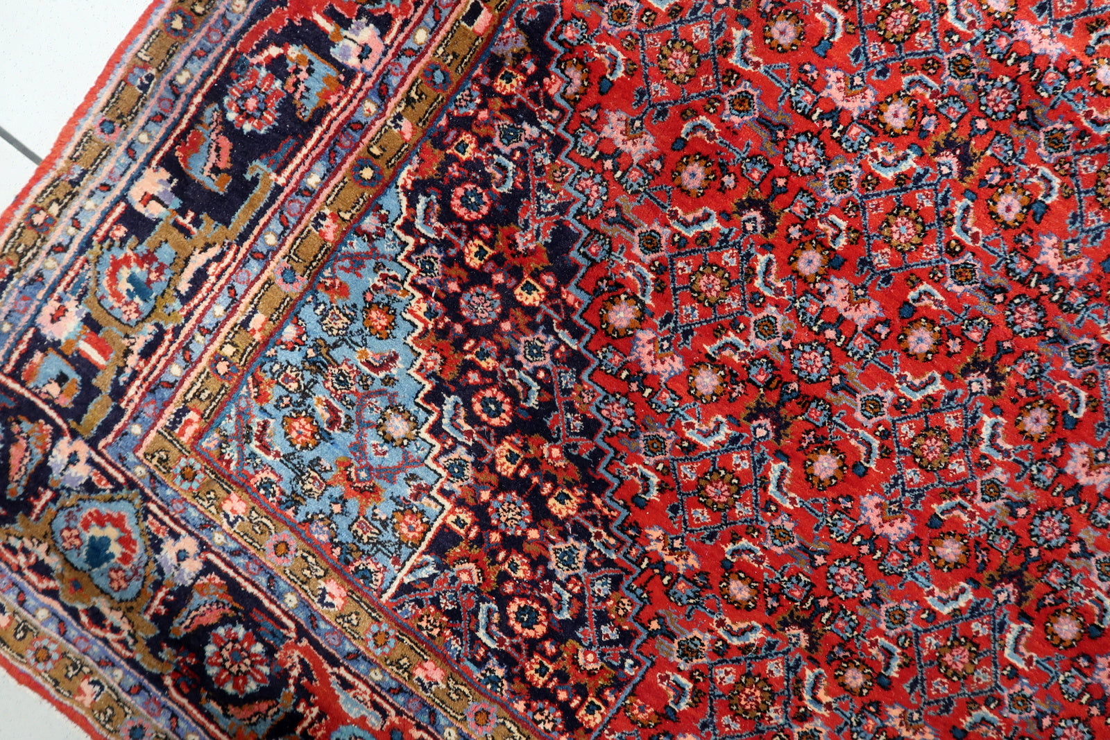 Close-up of the central diamond medallion on an antique Persian Bidjar rug, featuring sky blue and ivory tones against madder red.

