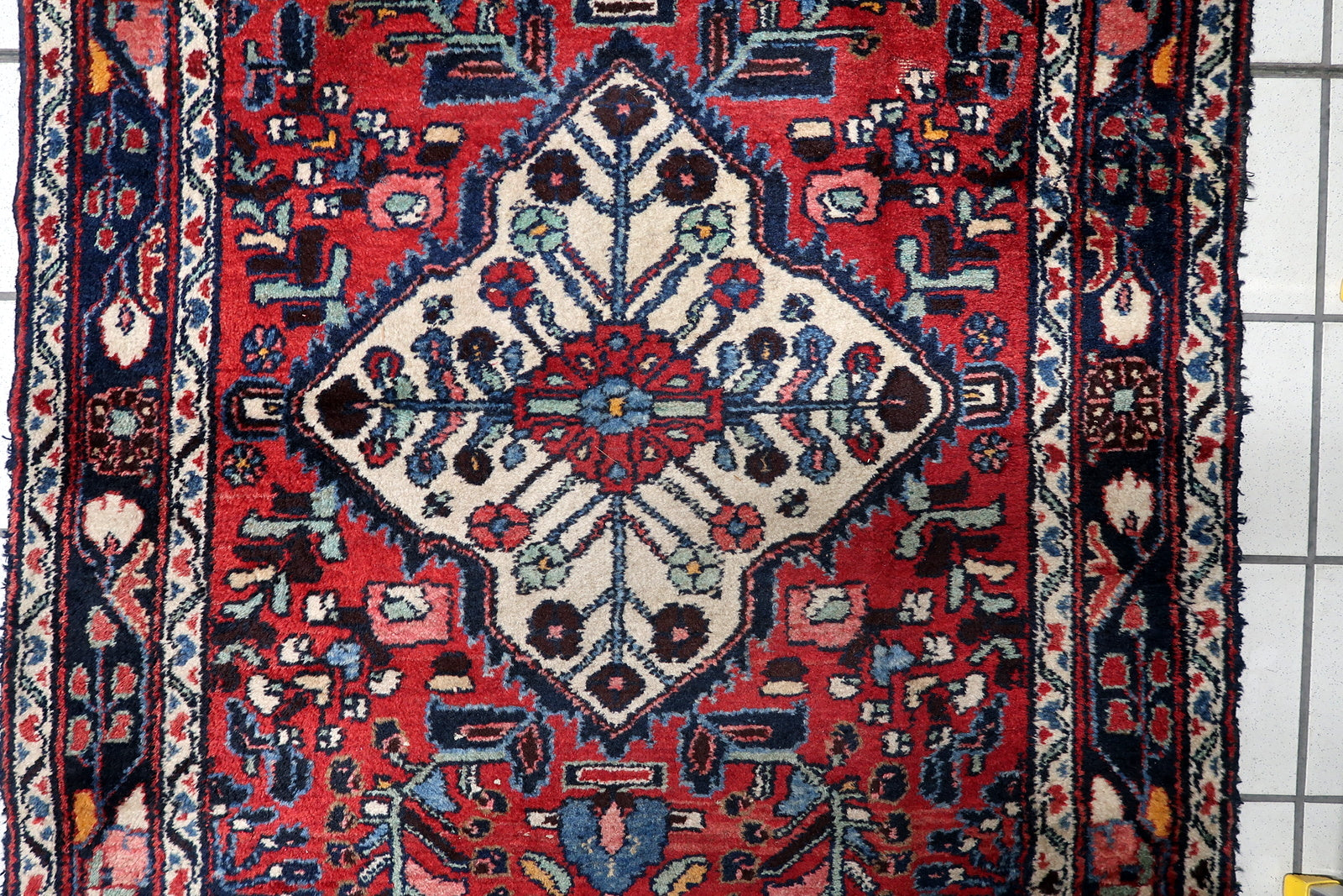 Close-up of a primary ivory diamond medallion on an antique Persian Hamadan runner, surrounded by angular floral sprays and geometric motifs.

