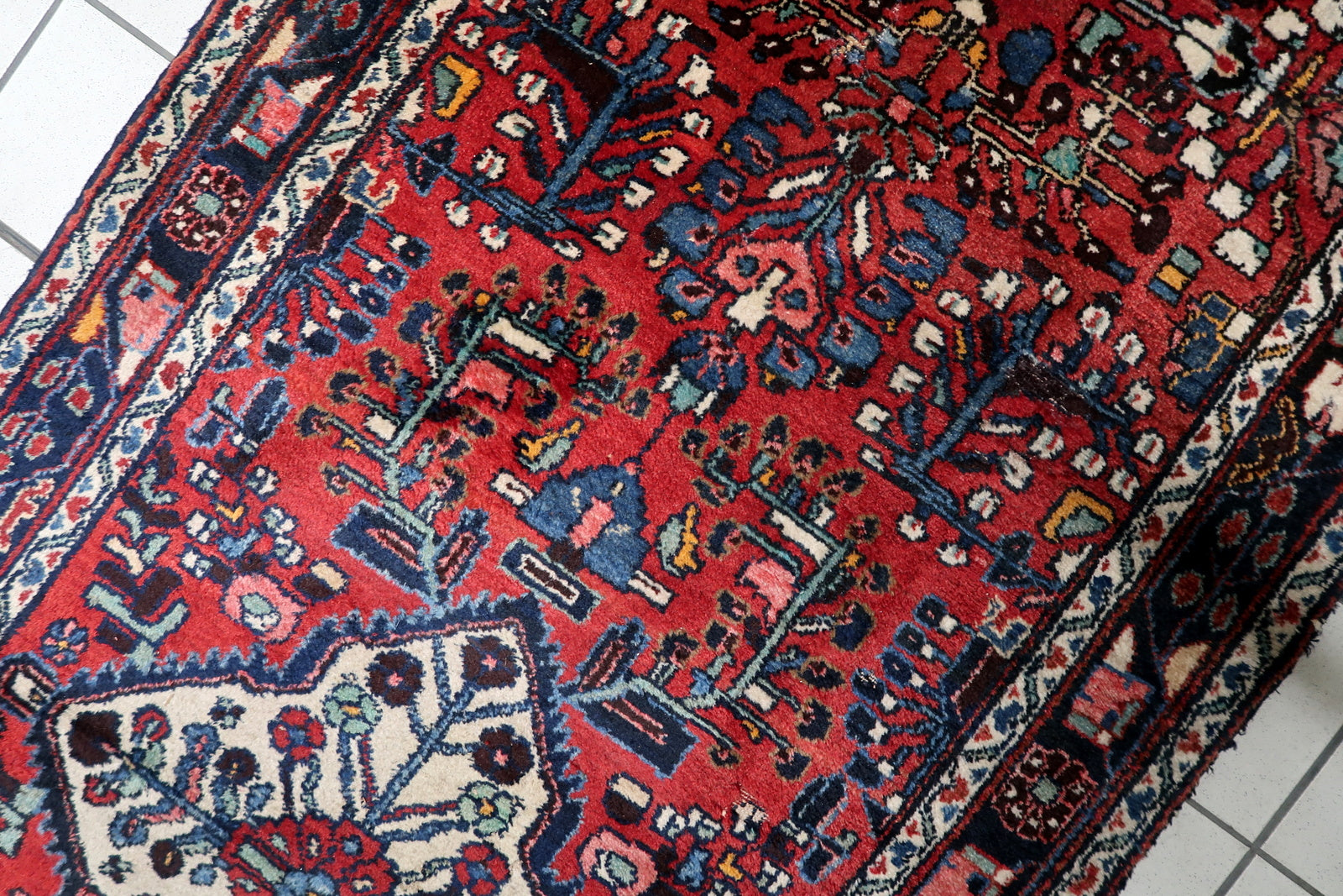 Detail of the vibrant color palette on a 1920s Hamadan runner: madder red, midnight blue, ivory, sage green, and ochre.

