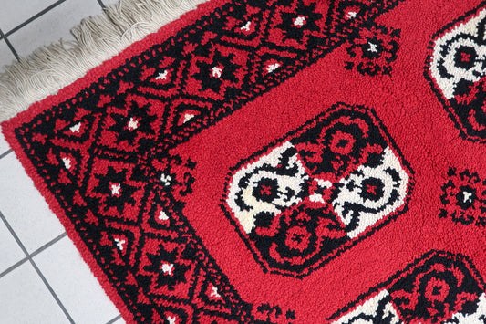 Vintage French rug with a bold modernist aesthetic, showcasing two rows of five black and cream octagonal "guls" against vibrant scarlet. 4'9" x 7'7".

