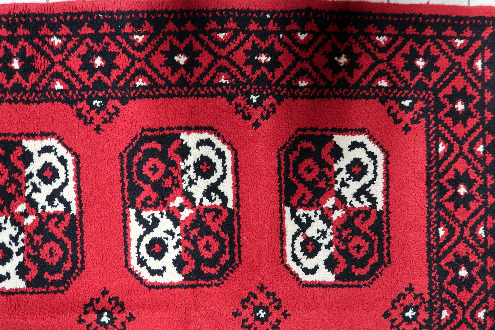 Close-up of a graphic octagonal medallion (gul) on a mid-century French rug, rendered in high-contrast black and cream on a scarlet field.

