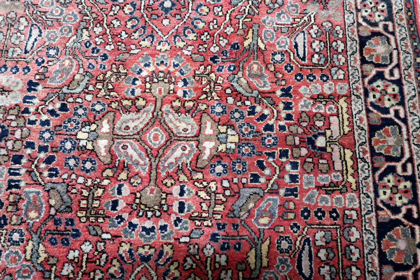 The vibrant madder-red field of a mid-century Hamadan rug, densely populated with midnight blue and ivory Herati motifs.

