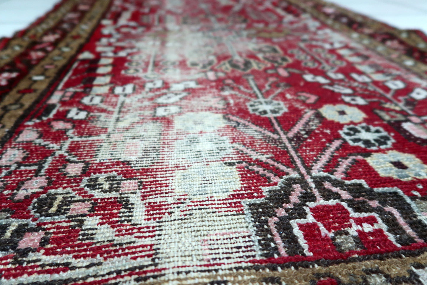 Deep crimson field of an antique Persian rug decorated with geometric tribal patterns in contrasting earth tones.

