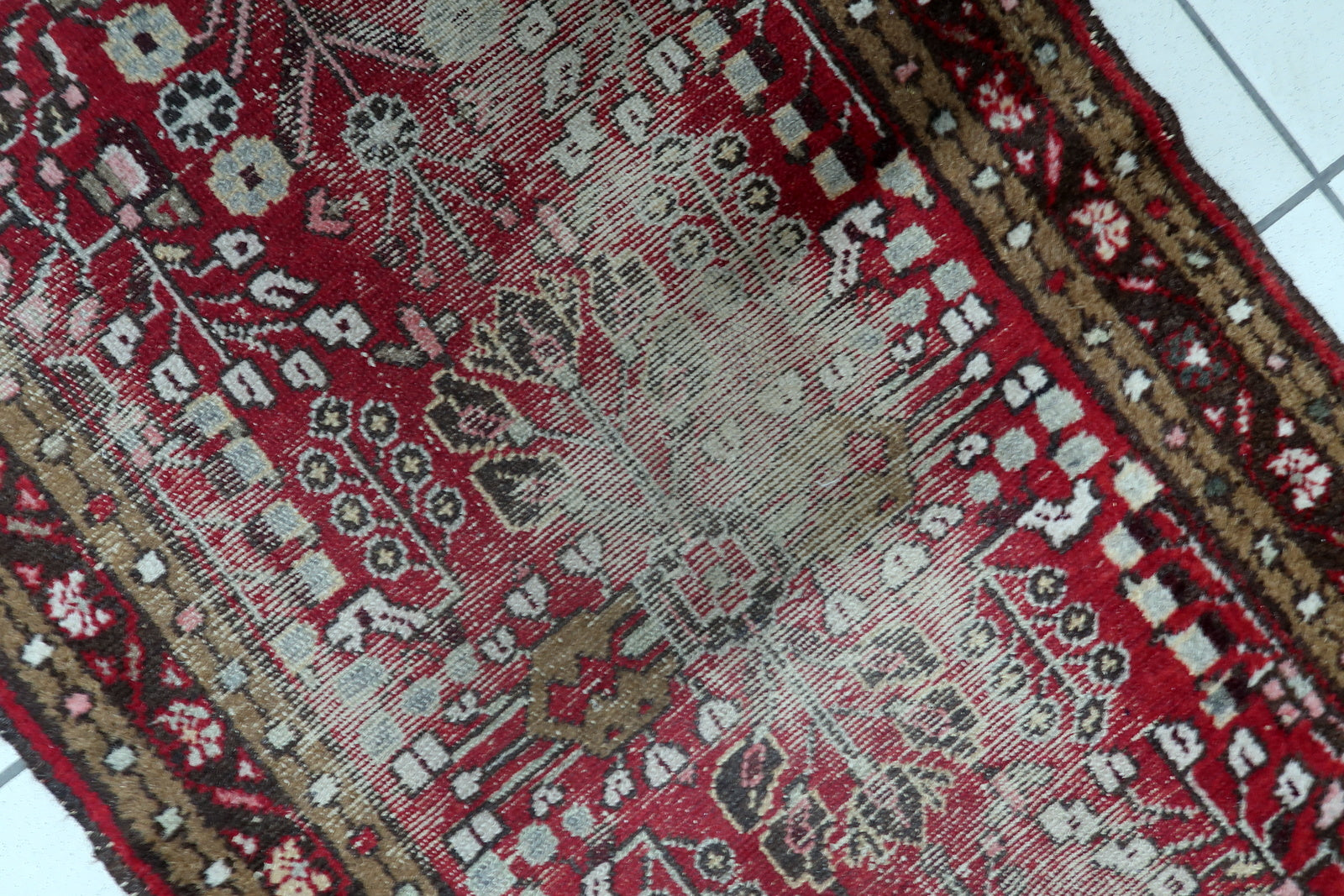 Close-up of stylized, angular floral and geometric motifs on a 1920s Persian Hamadan rug, characteristic of village weaving traditions.

