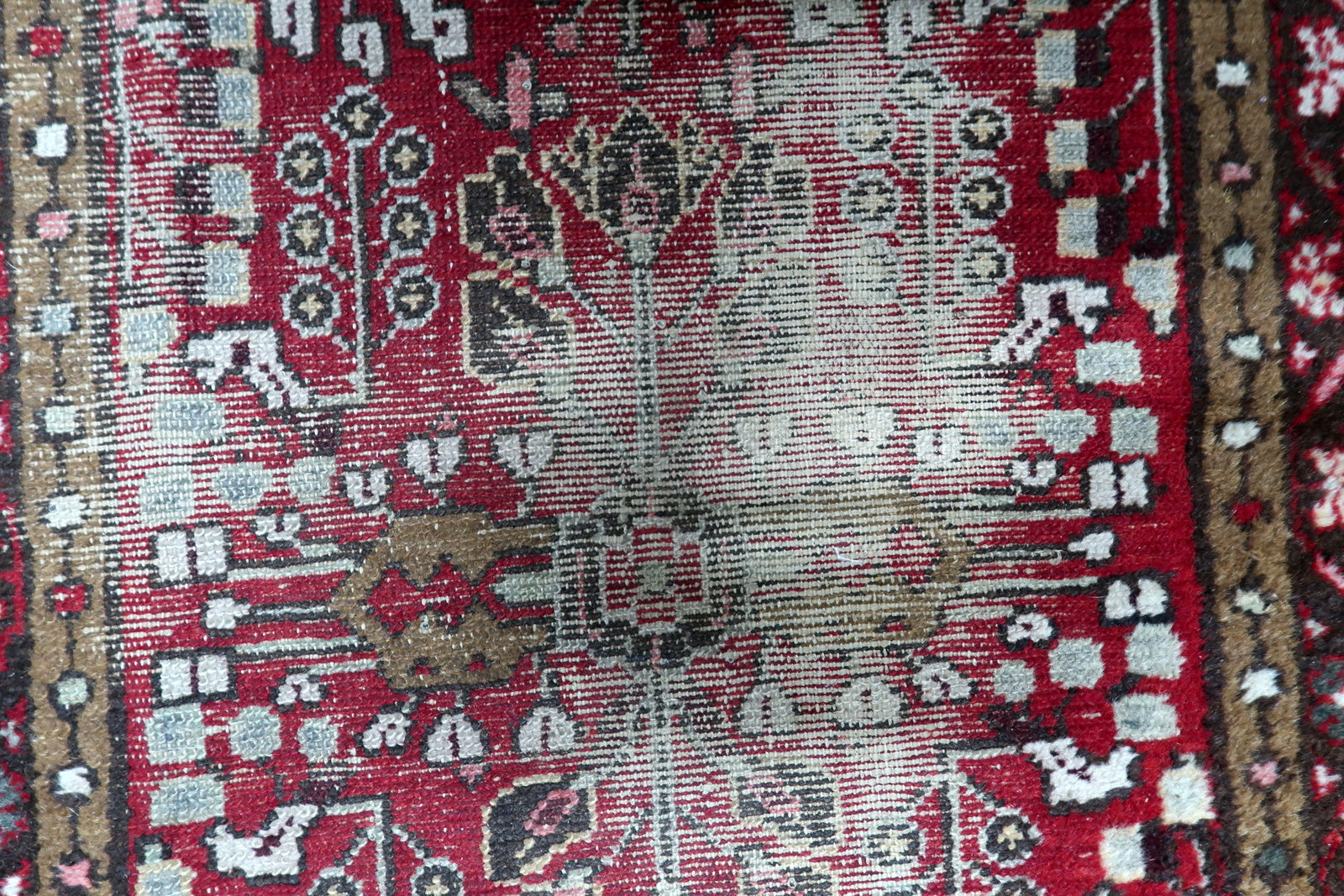 Detail of the distressed aesthetic on an antique rug, showing visible wear and low-to-absent pile that reveals the structural soul.

