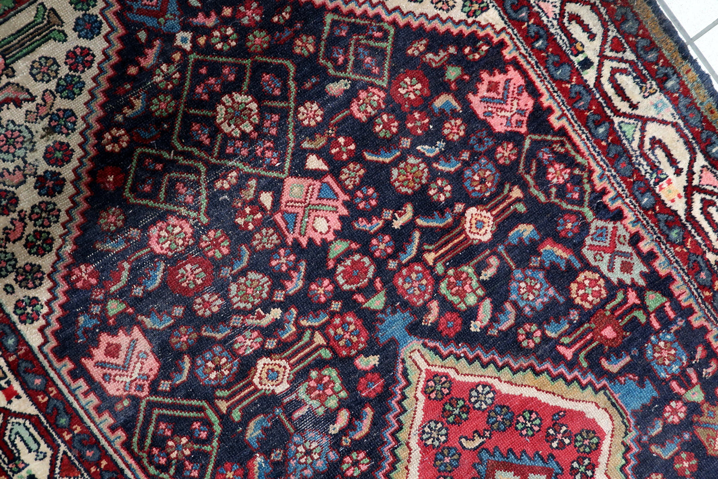 Handmade antique Hamadan carpet circa 1920s, showcasing contrasting ivory spandrels filled with delicate rose and green blossoms.

