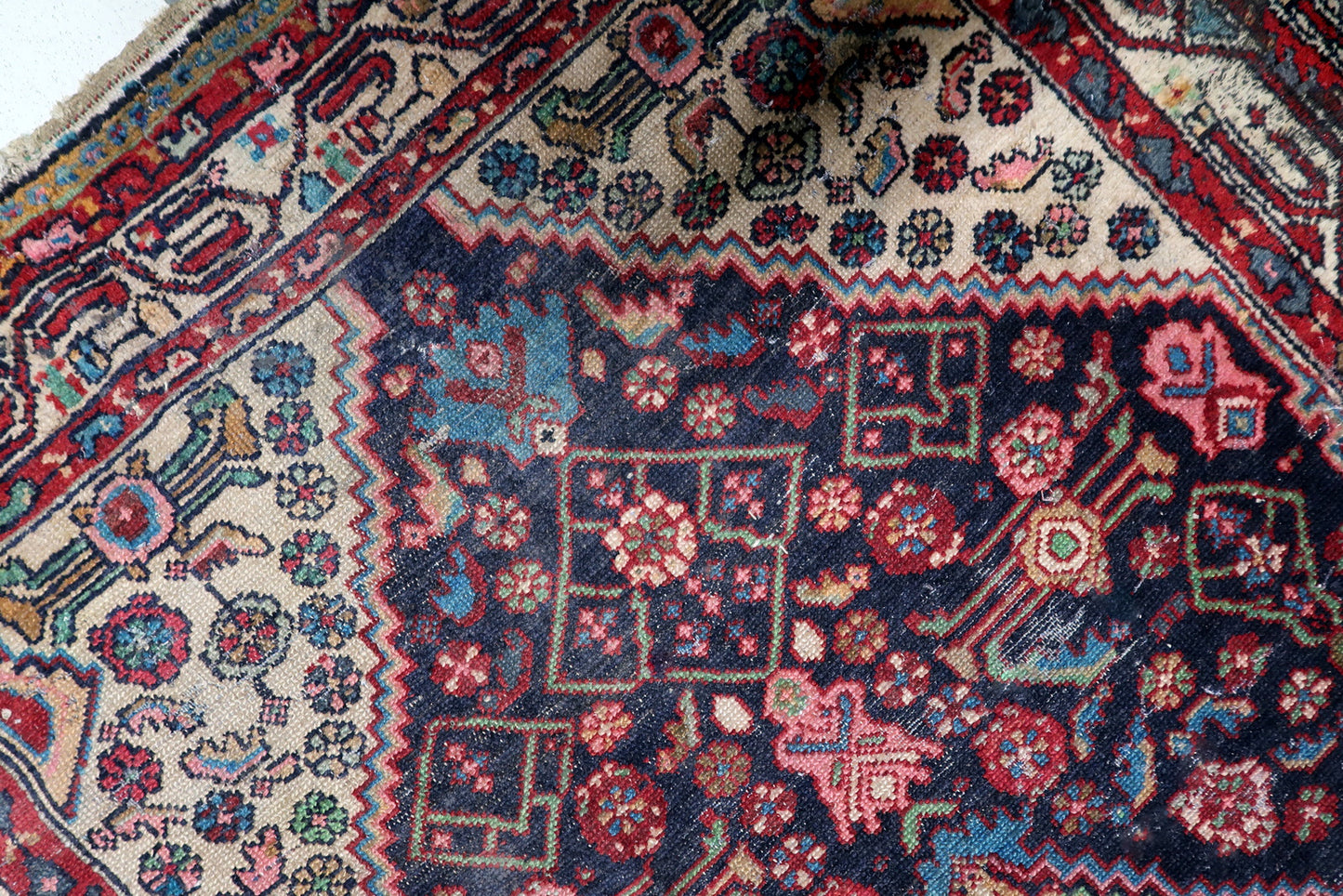 Detail of contrasting ivory corner spandrels on an antique Persian rug, featuring delicate stylized rose and green floral blossoms.

