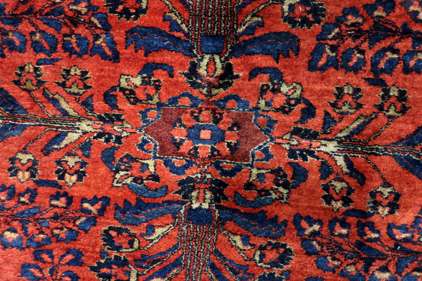 Detail of the sophisticated navy blue border on an antique "American Sarouk" style rug, showing a repeating floral vine motif.

