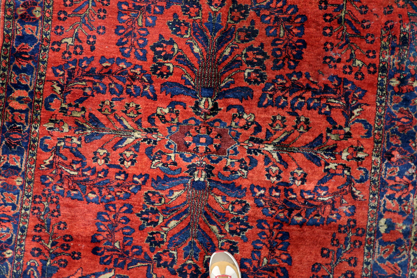 The rich madder-red field of a Persian Lilihan carpet, serving as a dramatic backdrop for deep navy, teal, and soft gold botanicals.

