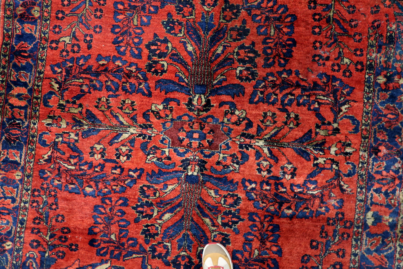 The rich madder-red field of a Persian Lilihan carpet, serving as a dramatic backdrop for deep navy, teal, and soft gold botanicals.

