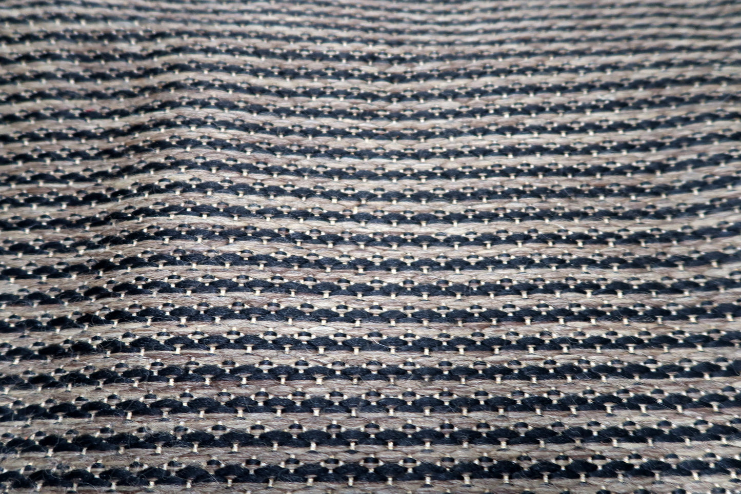 The wide pebbled charcoal border of a Belgian minimalist rug, providing a strong architectural frame for the geometric interior.

