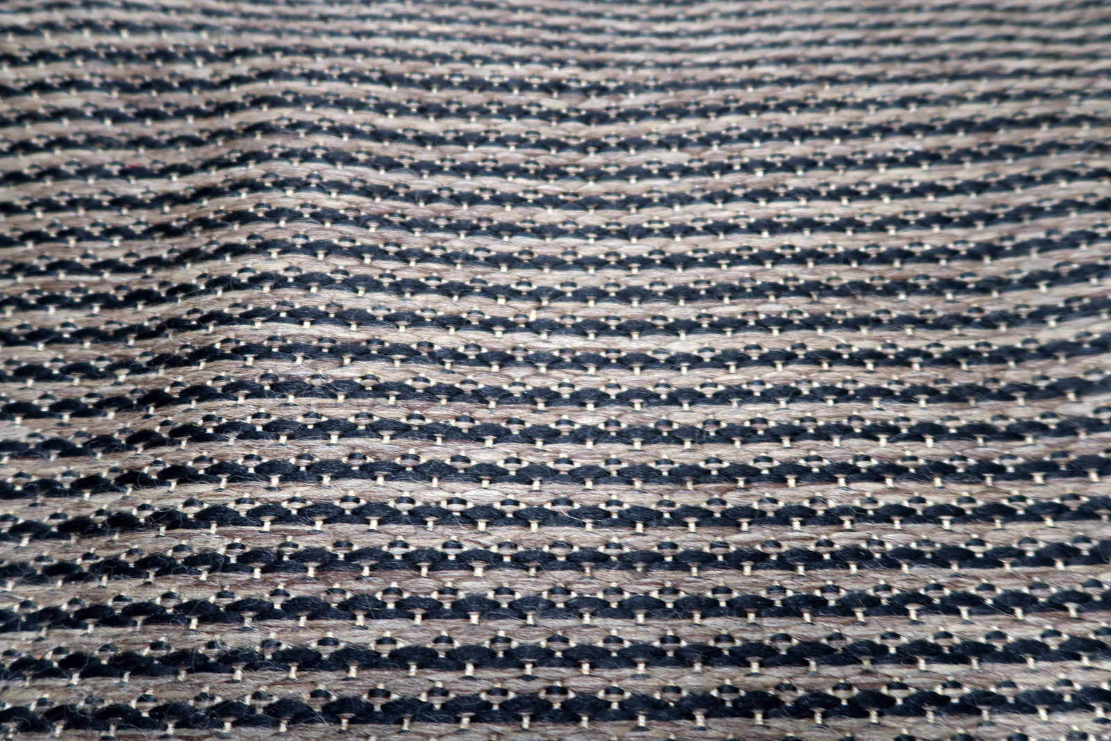 The wide pebbled charcoal border of a Belgian minimalist rug, providing a strong architectural frame for the geometric interior.

