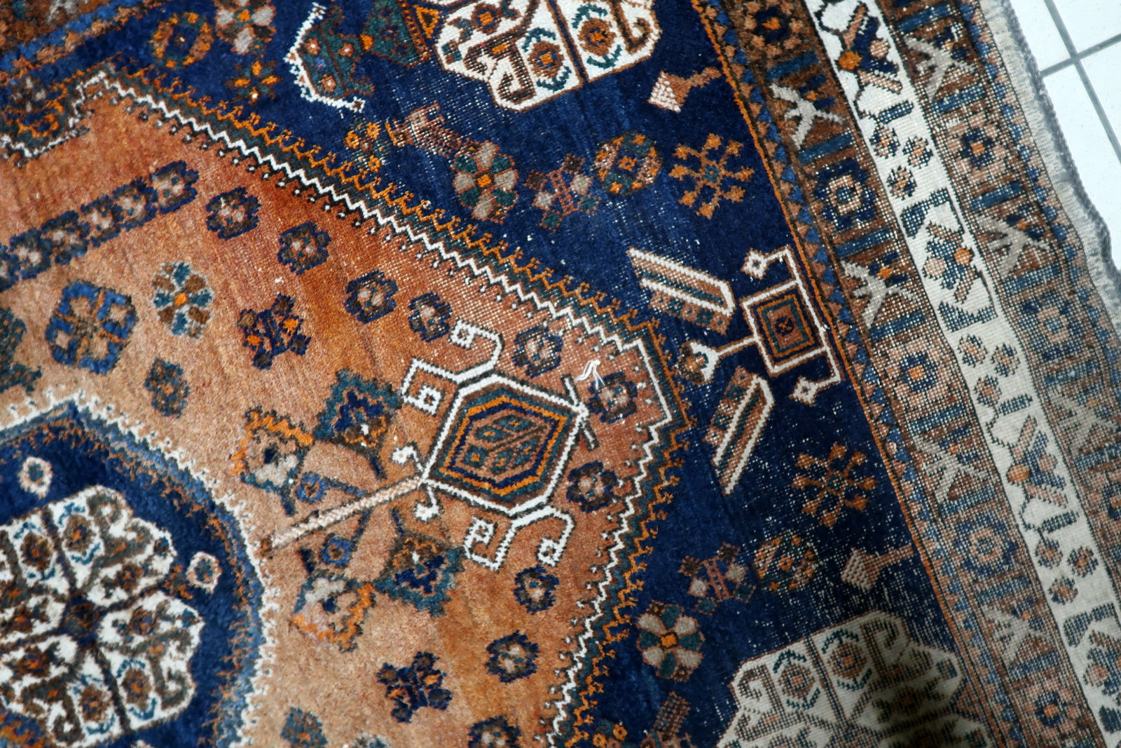 Handmade antique Gashkai carpet circa 1920s, showcasing striking ivory corner spandrels and a traditional multi-banded border in distressed condition.

