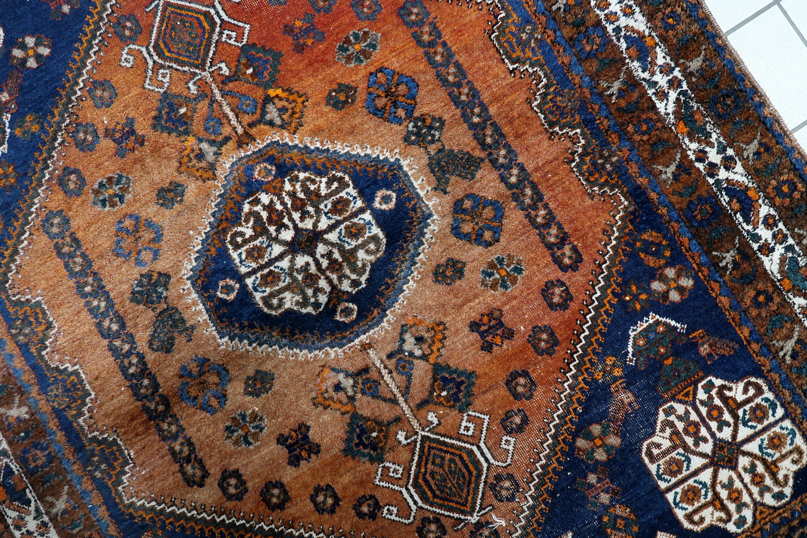Close-up of the prominent elongated hexagonal medallion on a 1920s Shiraz Gashkai rug, densely packed with ancient tribal symbols.

