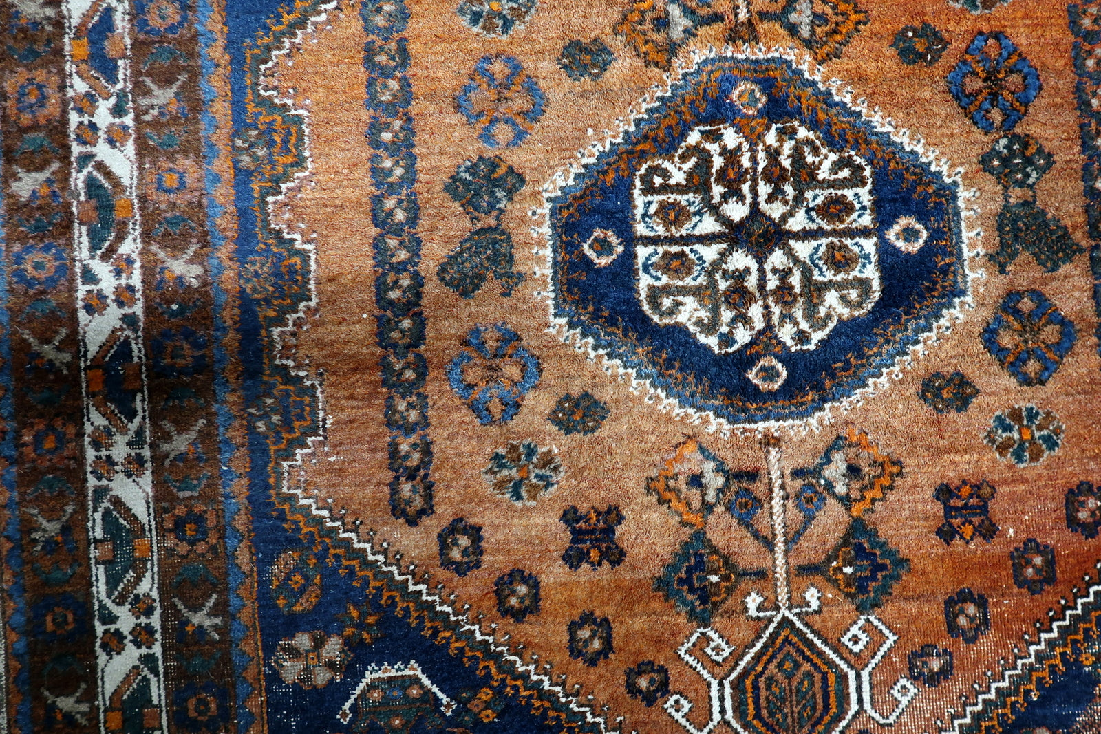 Detail of striking ivory corner spandrels providing crisp contrast to the warm terracotta-orange and midnight-blue tones of a nomadic Persian rug.


