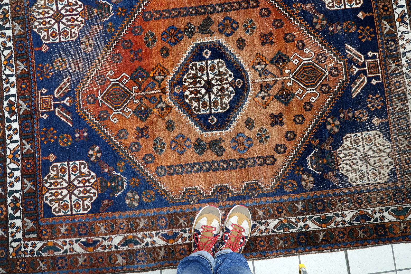 A 1920s nomadic tribal carpet with distressed character, ideal for layering in a modern interior or as a statement piece in a traditional dining area.

