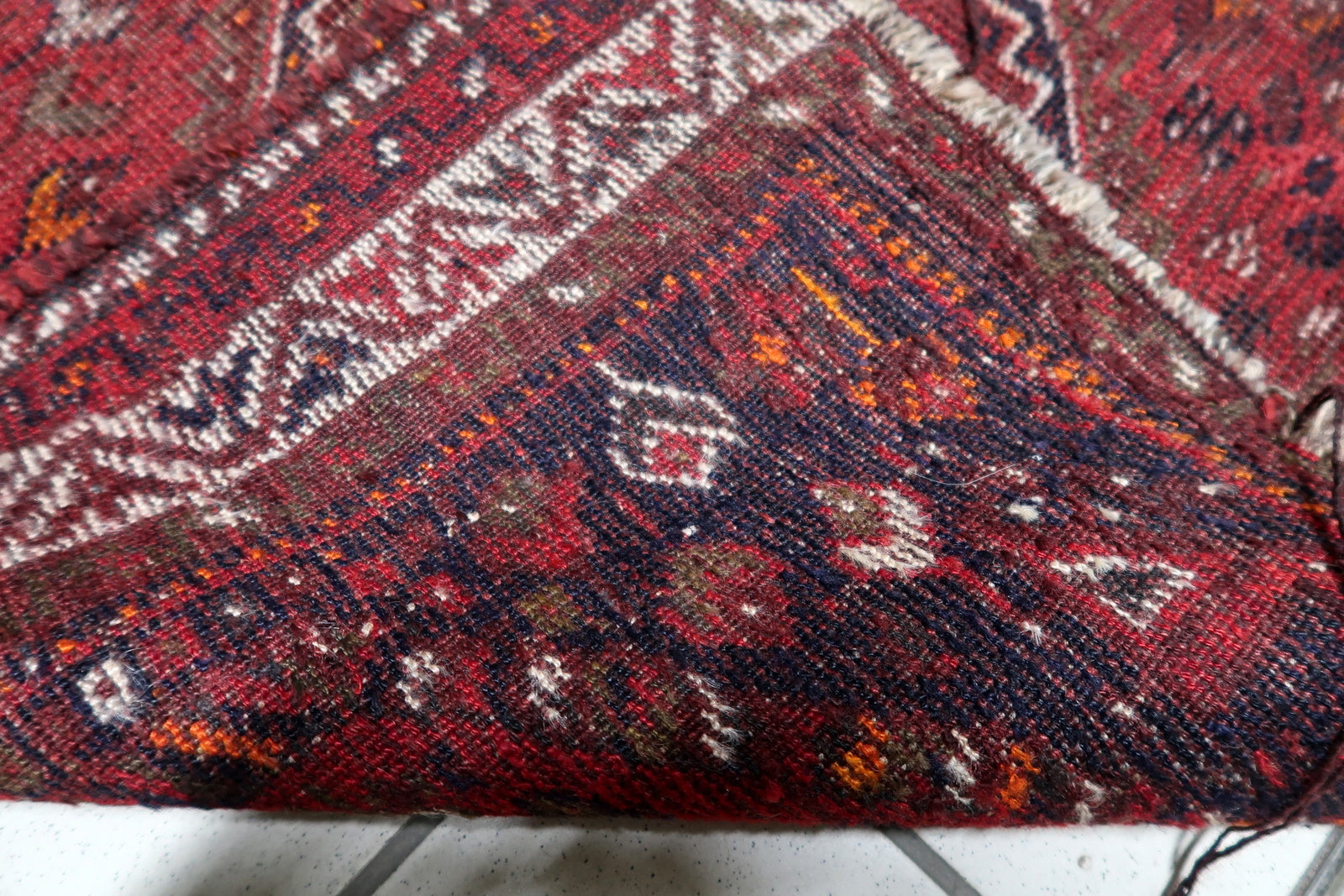 Small antique rug in oxblood red, suitable as a bedside accent, wall hanging, or layered over a larger neutral carpet.

