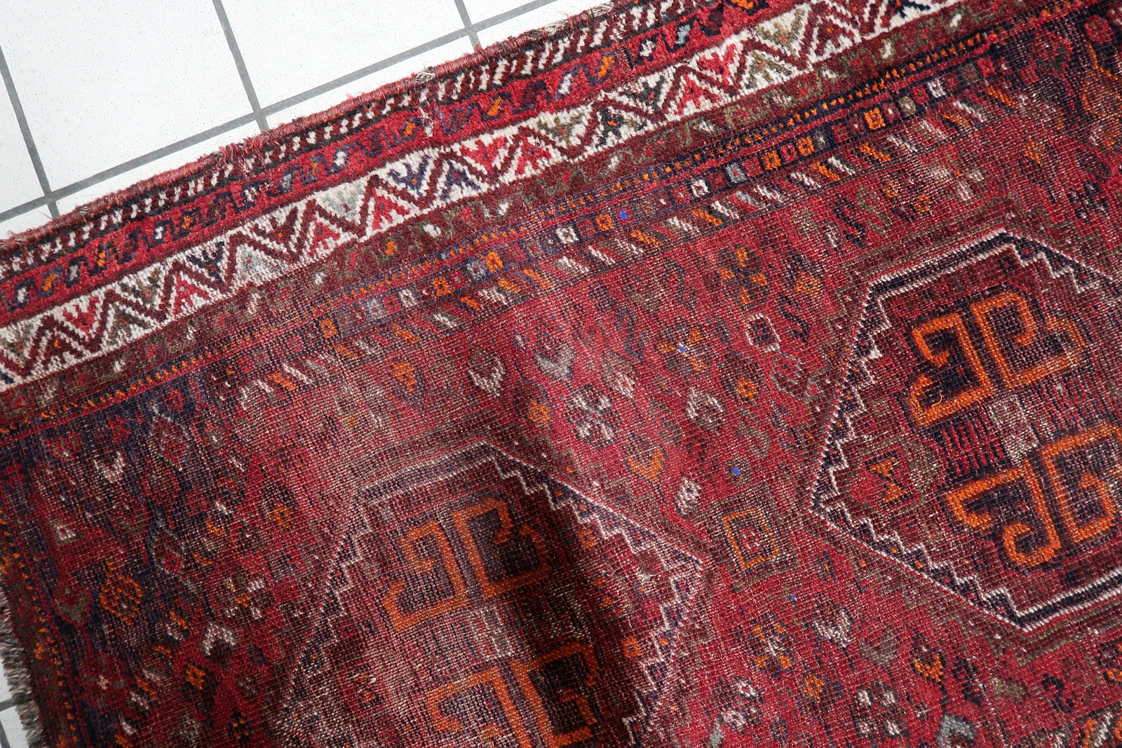 Close-up of the two primary diamond medallions on a 1900s Persian Shiraz rug, featuring archaic hooked "S" motifs and geometric tribal symbols.


