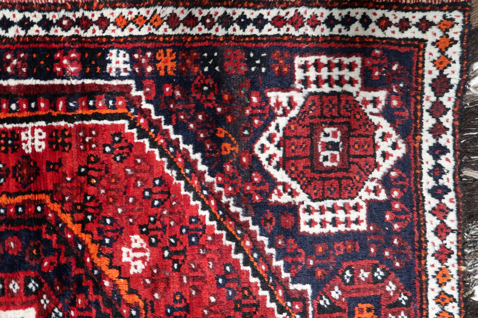 Close-up of intricate tribal motifs and geometric stars on a vintage hand-knotted Persian Shiraz carpet.

