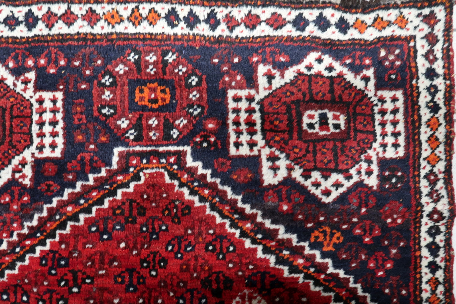Full view of an antique Persian Shiraz rug showing navy and ivory geometric medallions against a rich red background.

