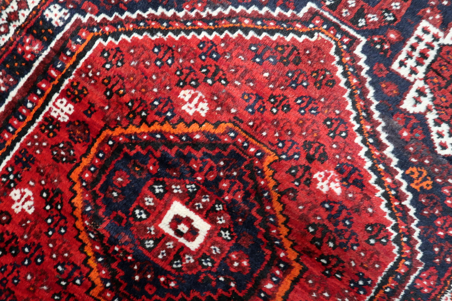 Detailed border pattern of an antique Persian rug featuring classic repeating vine and petal motif in navy and red.

