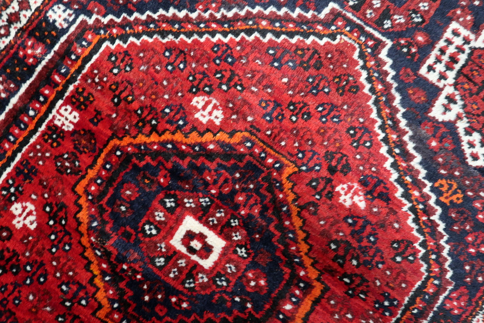 Detailed border pattern of an antique Persian rug featuring classic repeating vine and petal motif in navy and red.

