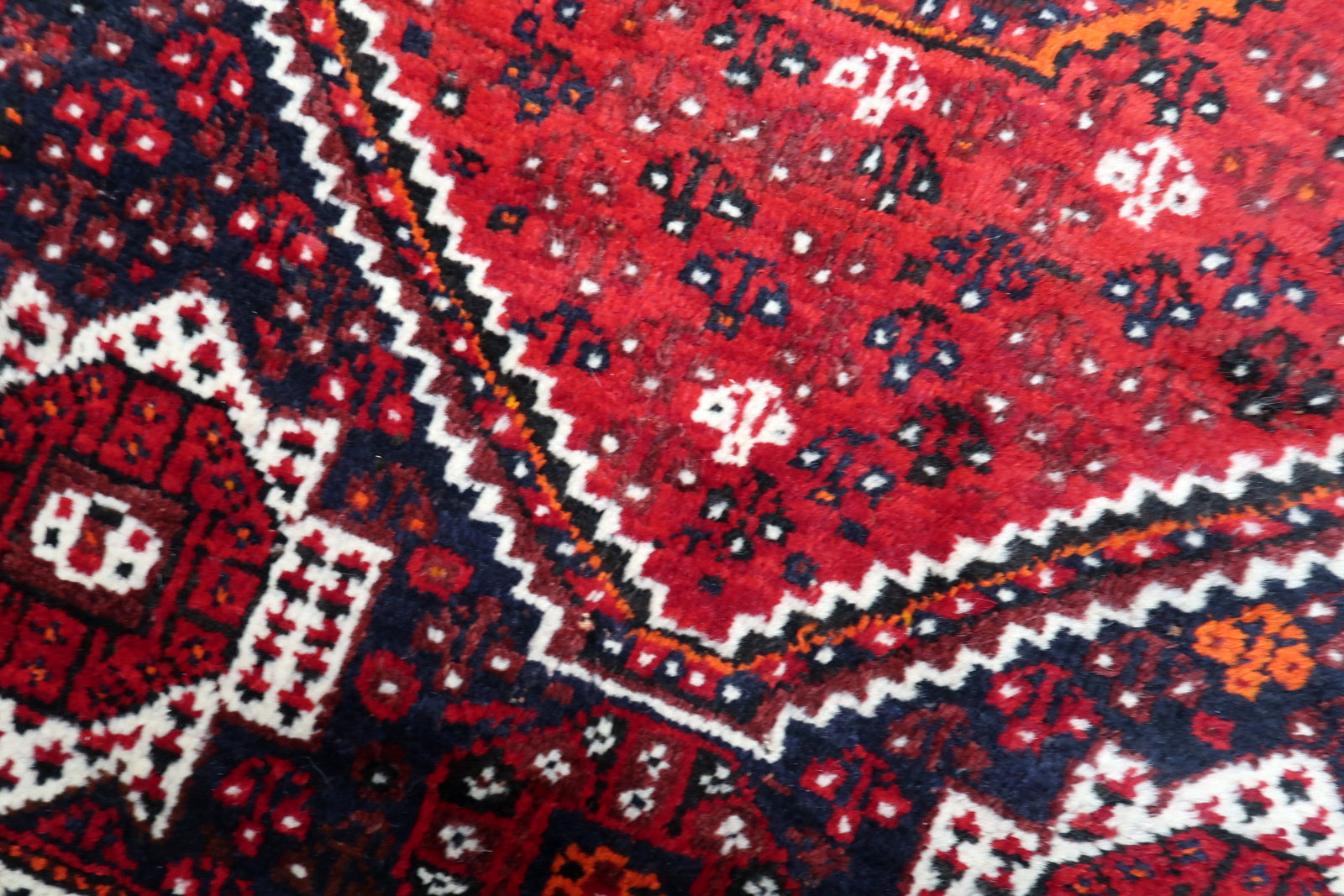 Red, navy blue and ivory antique Persian rug with tribal nomadic weaving symbols and floral heads.
