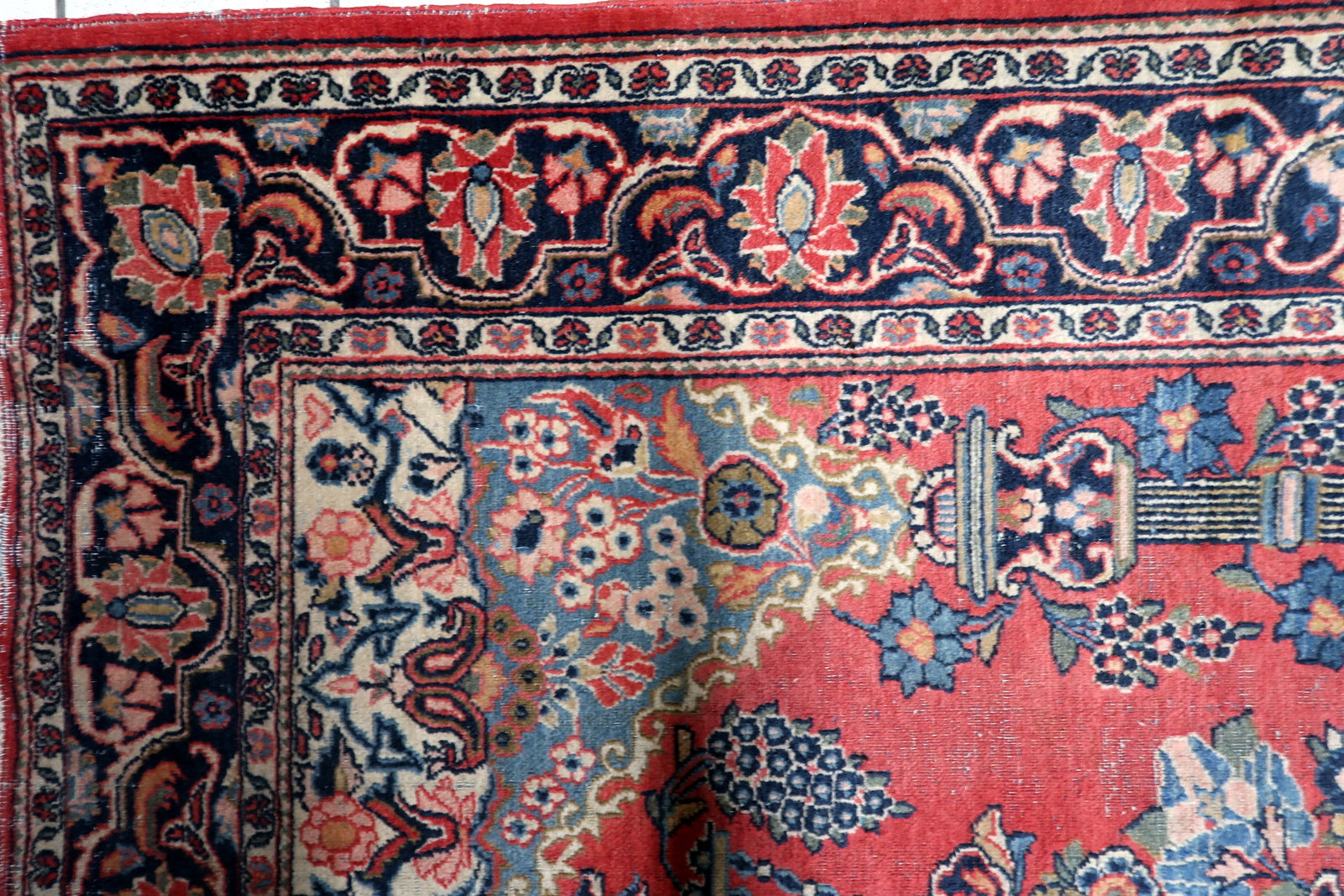Close-up of ornate floral vase and symmetrical blossoming vines on a vintage hand-knotted Persian Kashan carpet.

