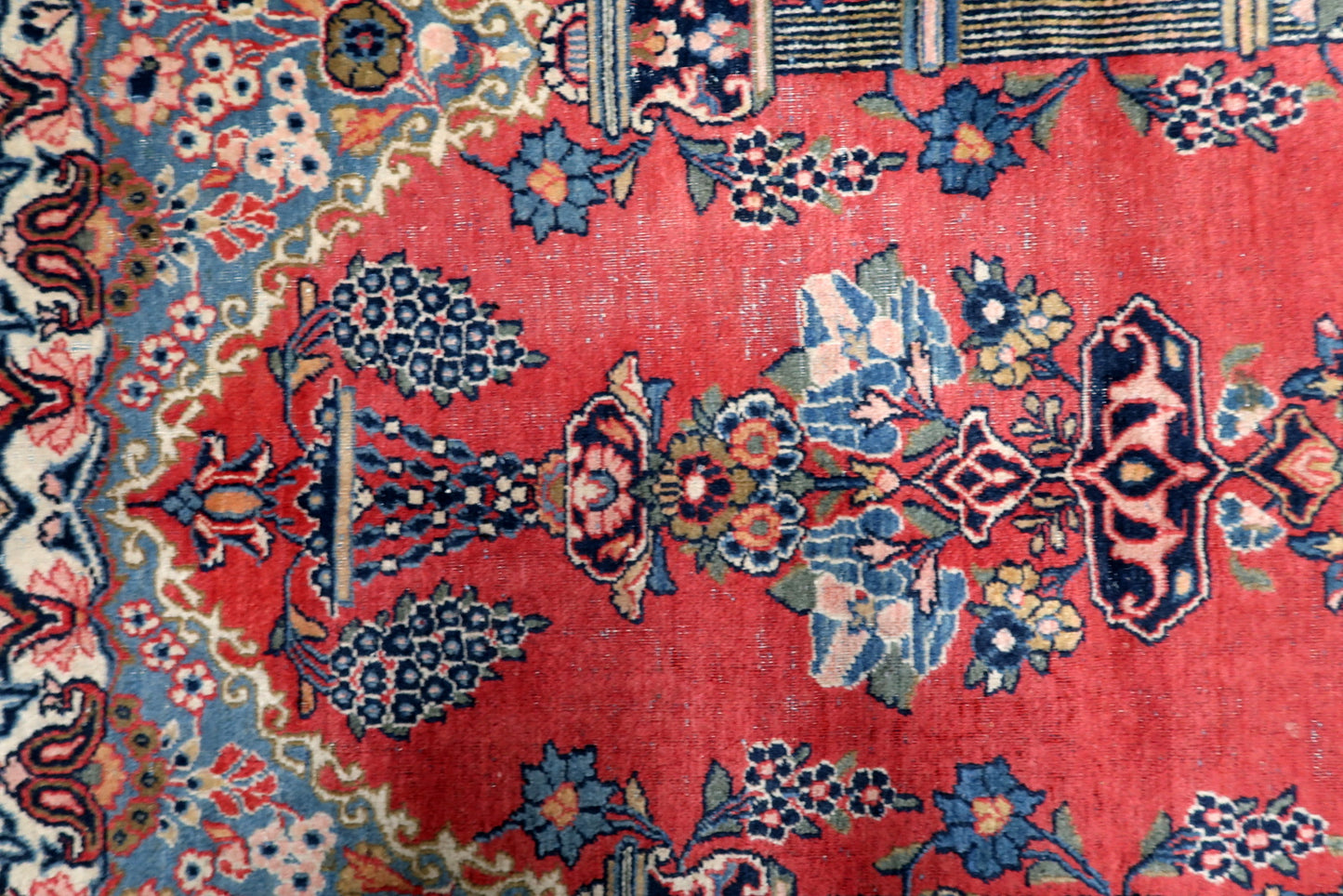 Detailed sky-blue spandrels of a 1920s Kashan rug featuring delicate floral sprays contrasting with the primary field.

