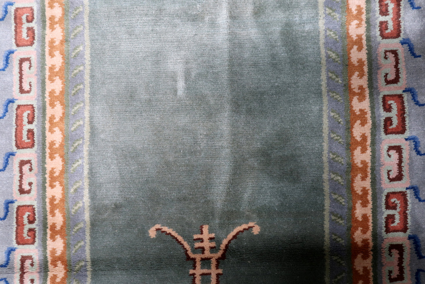 Detailed main border of a vintage Art Deco rug showing terracotta and navy blue fretwork pattern against slate-grey background