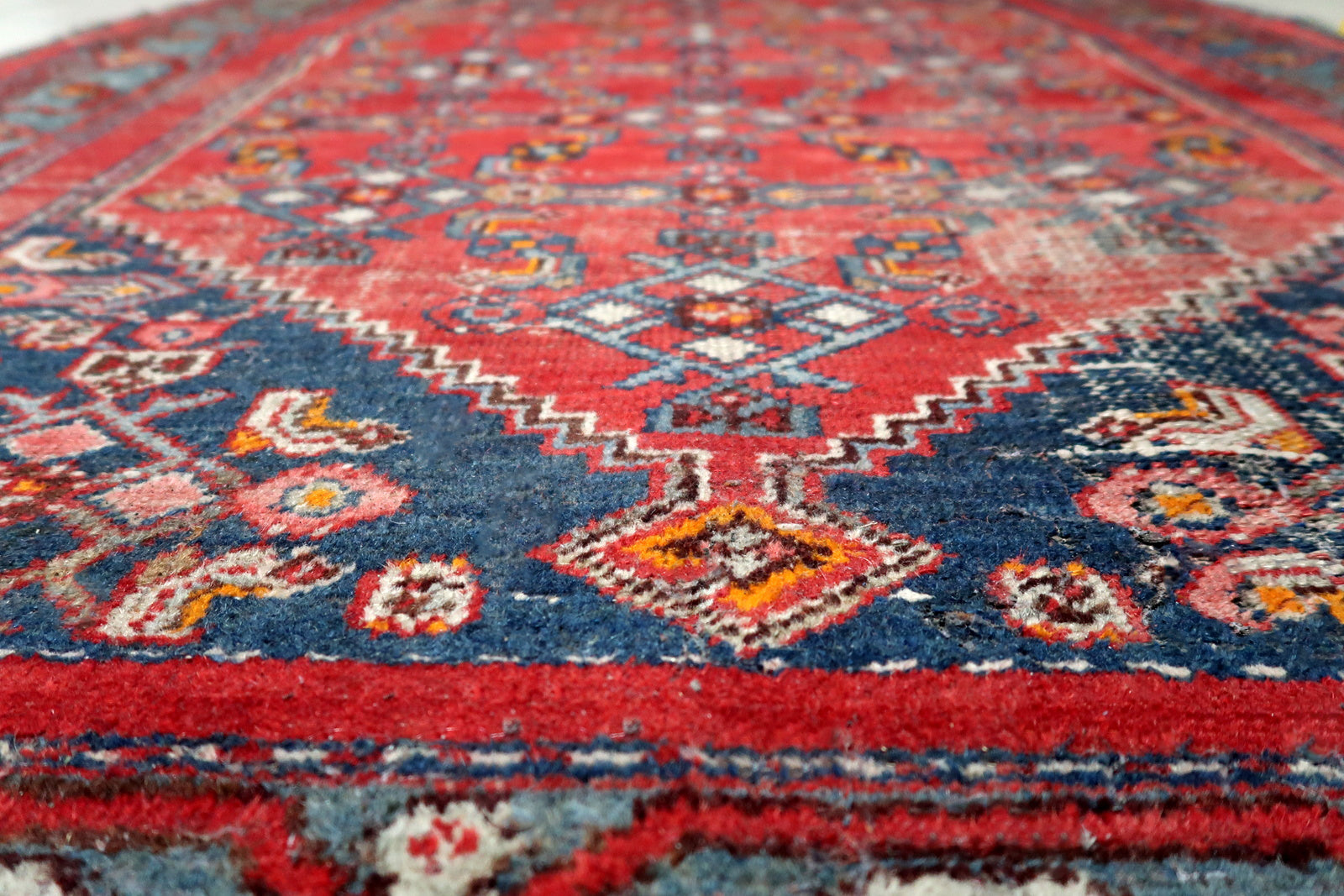 Antique Persian tribal rug with rich saturated red field and deep navy blue geometric spandrel designs